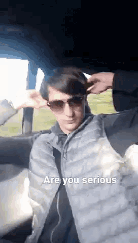 a man wearing sunglasses and a vest is sitting in a car with his hands on his ears .