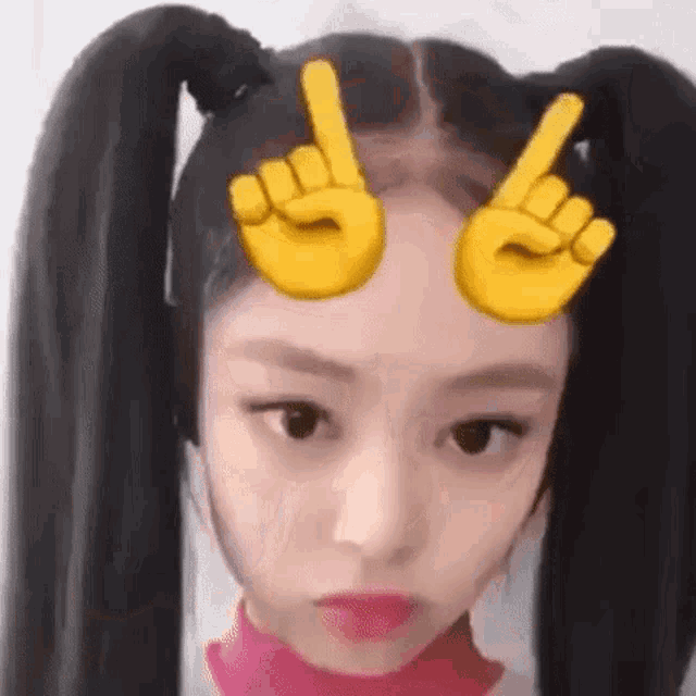 a girl with pigtails is wearing a filter with emoji hands on her forehead .