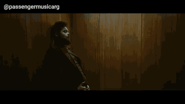 a man leaning against a wooden wall with passengermusicarg written on the bottom right