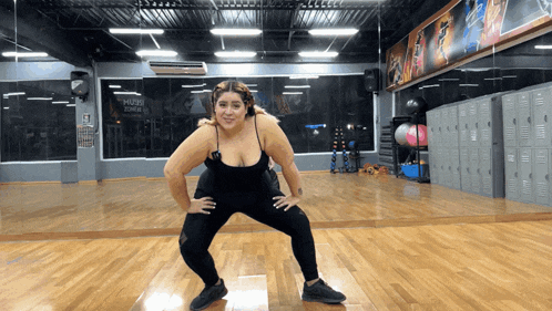 a woman is squatting in front of a mirror in a gym with a sign that says nutri zone
