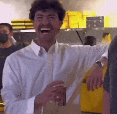 a man in a white shirt is laughing and holding a cup