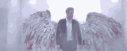 a man in a suit and white shirt is standing in a room with angel wings .