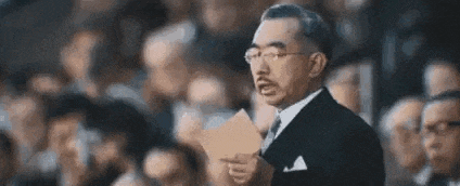 a man in a suit and tie is holding a piece of paper and giving a speech in front of a crowd .