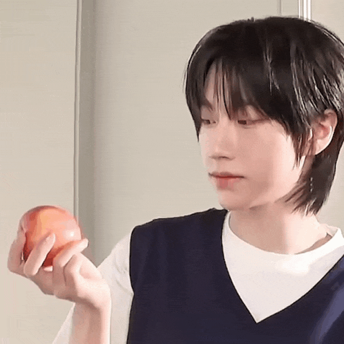a young man is holding an apple in his hand and looking at it .