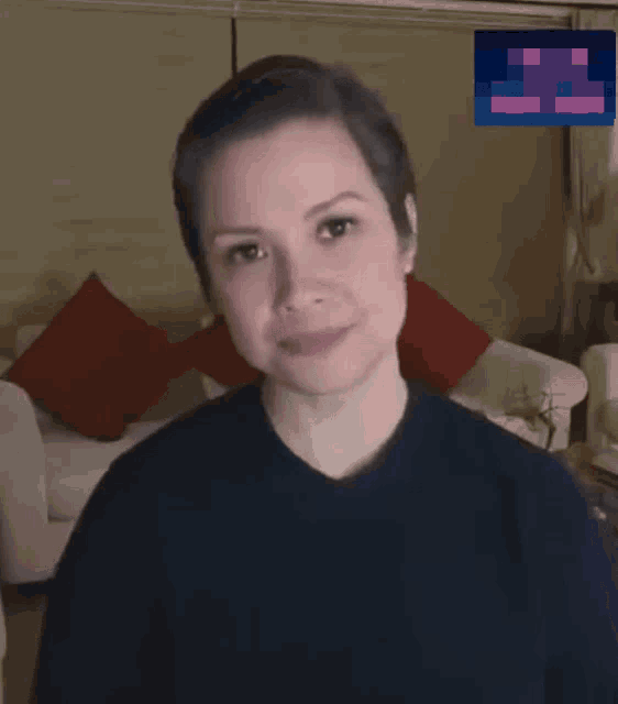 a woman with short hair is smiling in a living room with red pillows