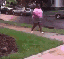 a woman in a pink shirt is walking down a sidewalk next to a car .