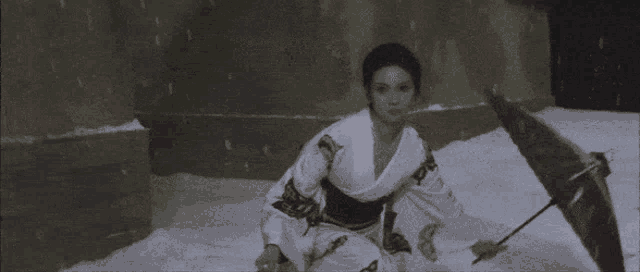 a woman in a kimono is sitting in the snow holding an umbrella