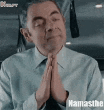 a man in a blue shirt and tie is praying with his hands folded .