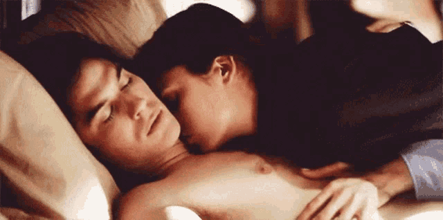 a man and a woman are laying in bed and the woman is kissing the man 's chest .