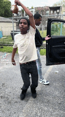 two young men are standing next to each other in front of a car and one is holding a bottle in his hand .