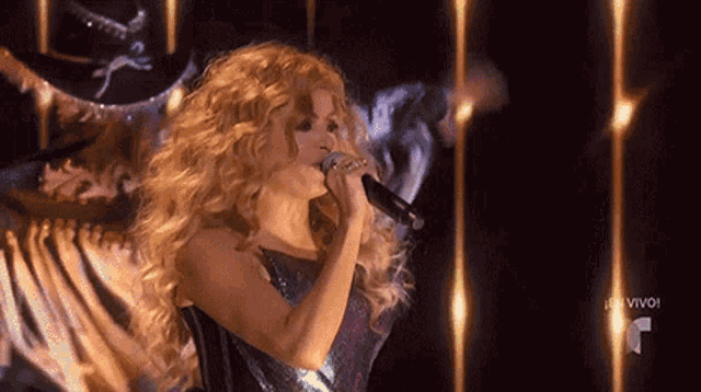 a woman singing into a microphone in front of a sign that says " vivo "