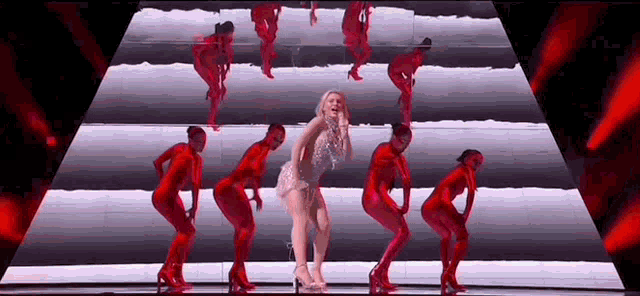 a woman is standing on a stage surrounded by dancers in red