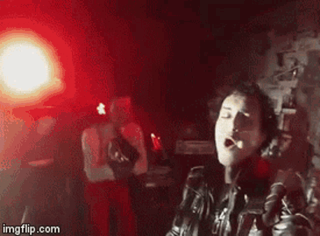 a man in a black leather jacket is smoking a cigarette while playing a guitar in a dark room .