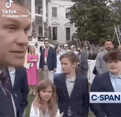 a man in a suit and tie is standing next to a group of children .