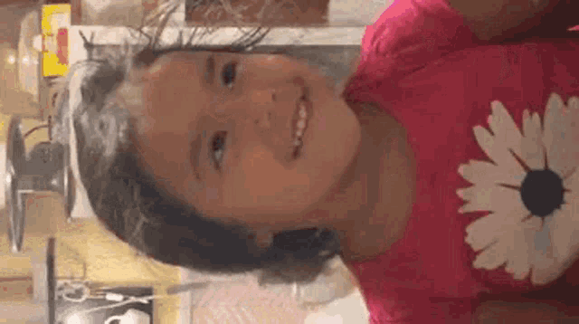 a little girl wearing a pink shirt with a flower on it is smiling .