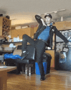 a man in a black hat is standing on one leg on a chair in a kitchen