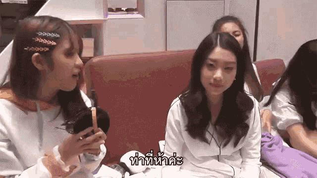 a group of girls are sitting on a couch talking to each other in a room .