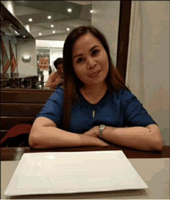 a woman in a blue shirt sits at a table with a white plate