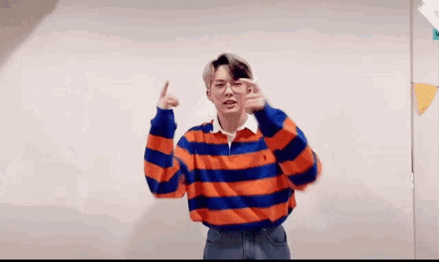a young man in a striped shirt is giving a thumbs up sign .