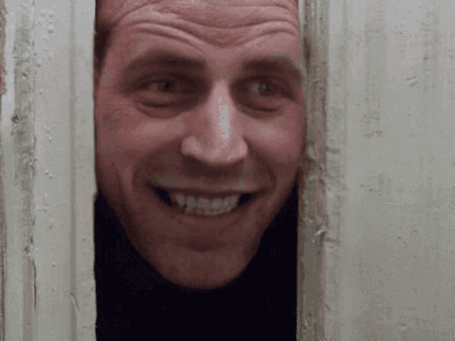 a man is smiling and looking through a door