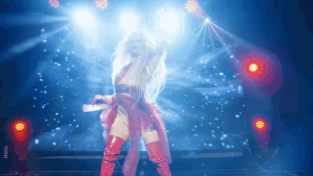 a woman in a red dress and red boots stands on a stage with her arms in the air