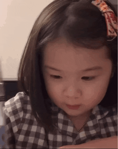 a little girl wearing a plaid shirt and a bow in her hair is looking down .