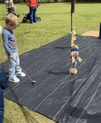 a young boy playing a game of golf with scarecrows in the background