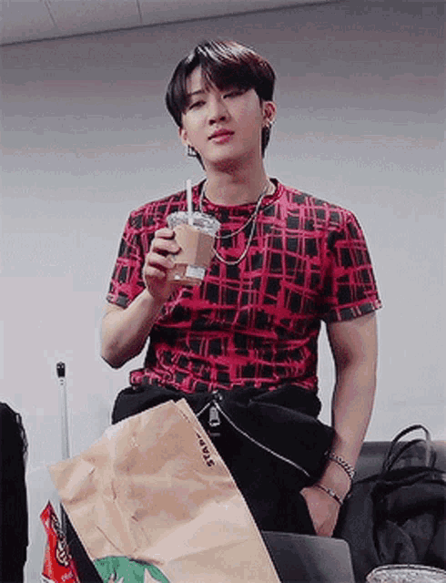a young man in a red shirt is holding a cup of coffee and a starbucks bag
