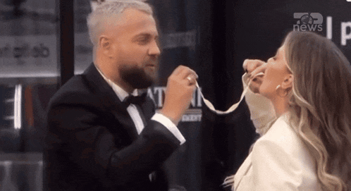 a man in a tuxedo is tying a woman 's hand with a ribbon