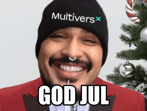 a man wearing a beanie that says multivers x is smiling in front of a christmas tree