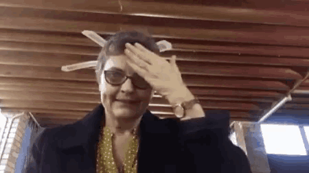 an elderly woman wearing glasses and a watch is covering her face with her hand .