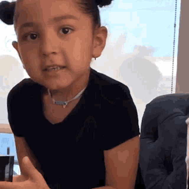 a little girl is wearing a black shirt and a necklace .
