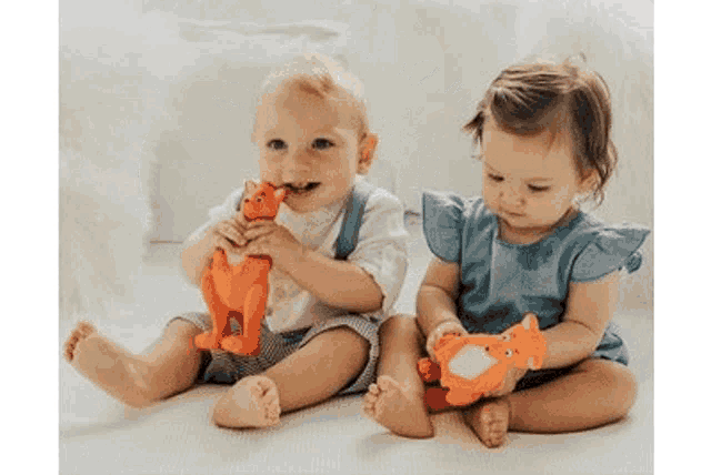 a baby boy and a baby girl are sitting on the floor holding toys .