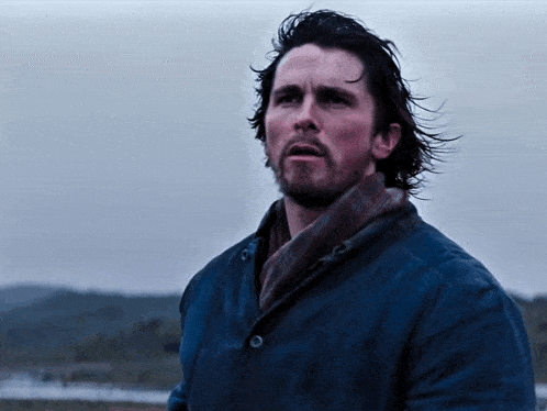 a man with long hair and a beard is wearing a blue coat