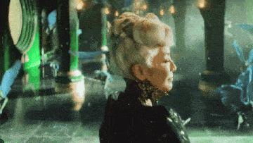a woman with white hair and a black dress stands in a room