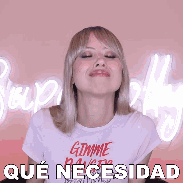a woman wearing a gimme dance t-shirt makes a face in front of a neon sign