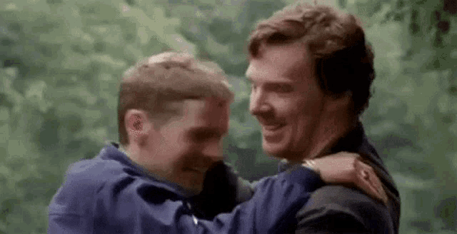 two men are hugging each other and smiling while standing next to each other in a park .