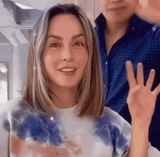 a woman is sitting in a chair with her hair cut by a hairdresser and waving at the camera .