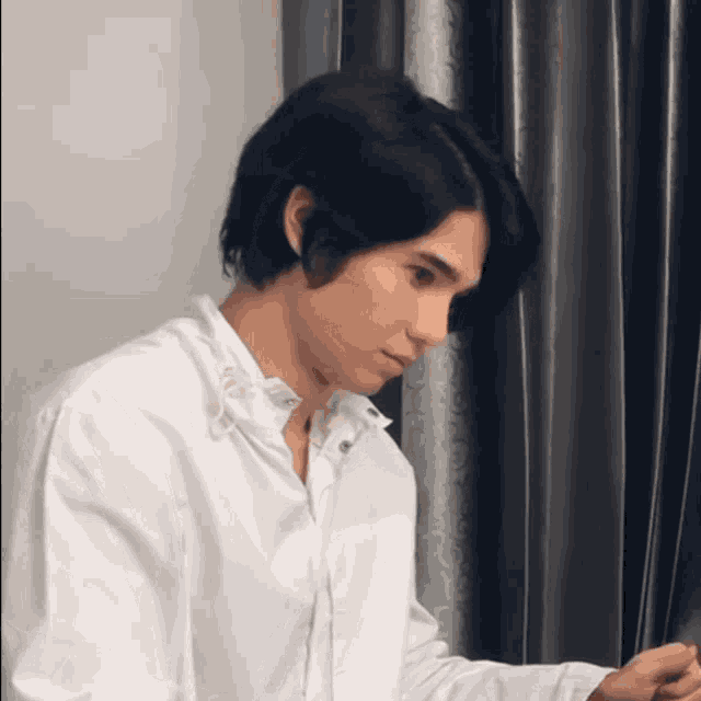 a young man in a white shirt is sitting in front of a curtain