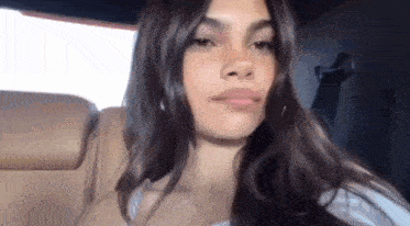 a woman with long dark hair is sitting in the back seat of a car and looking at the camera .
