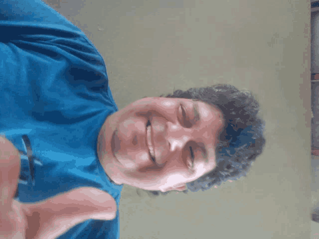 a man with curly hair wearing a blue shirt is smiling