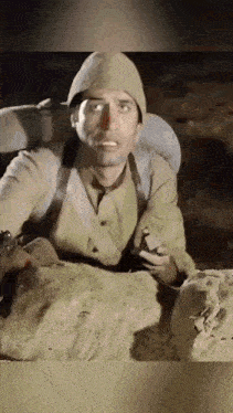 a man in a military uniform is sitting in a trench holding a cigarette .