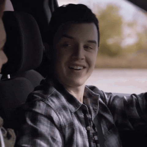 a man in a plaid shirt is sitting in the driver 's seat of a car