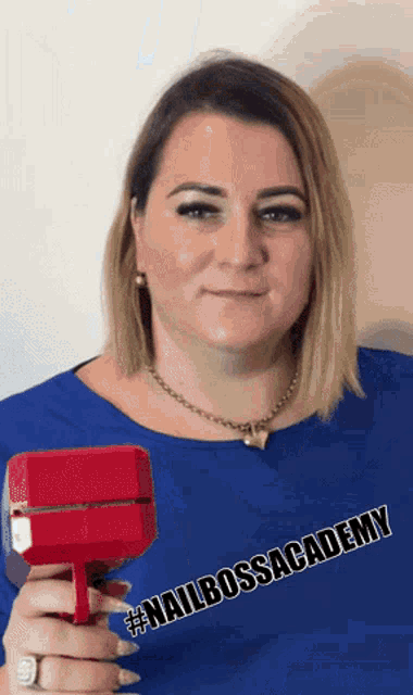 a woman wearing a blue shirt that says nail boss academy holds a red object