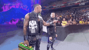 a wrestler with a punisher vest on talks to another wrestler