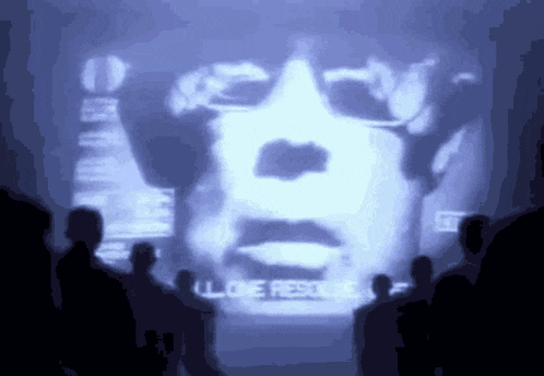a group of people are watching a projection of a man 's face with the words " i love rescue " written below it