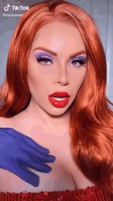 a woman with red hair and purple eyeshadow is wearing a wig and a blue glove .