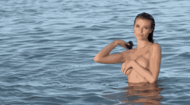 a naked woman is standing in the ocean with her hand up .
