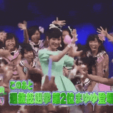 a girl in a green dress stands in front of a crowd with a sign that says " 2 "