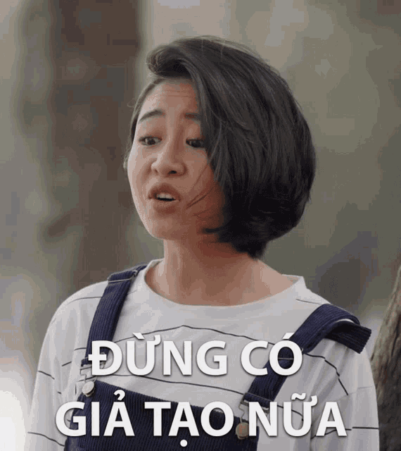 a girl with short hair is wearing overalls and a shirt that says dung co gia tao nữa